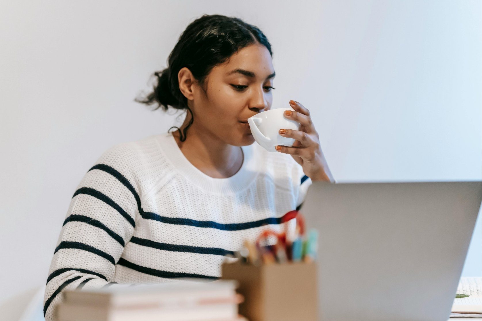 A woman sitting at a laptop drinking out of a cup